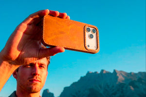 Ravenweave Honey leather iPhone case held outdoors, mountain scenery